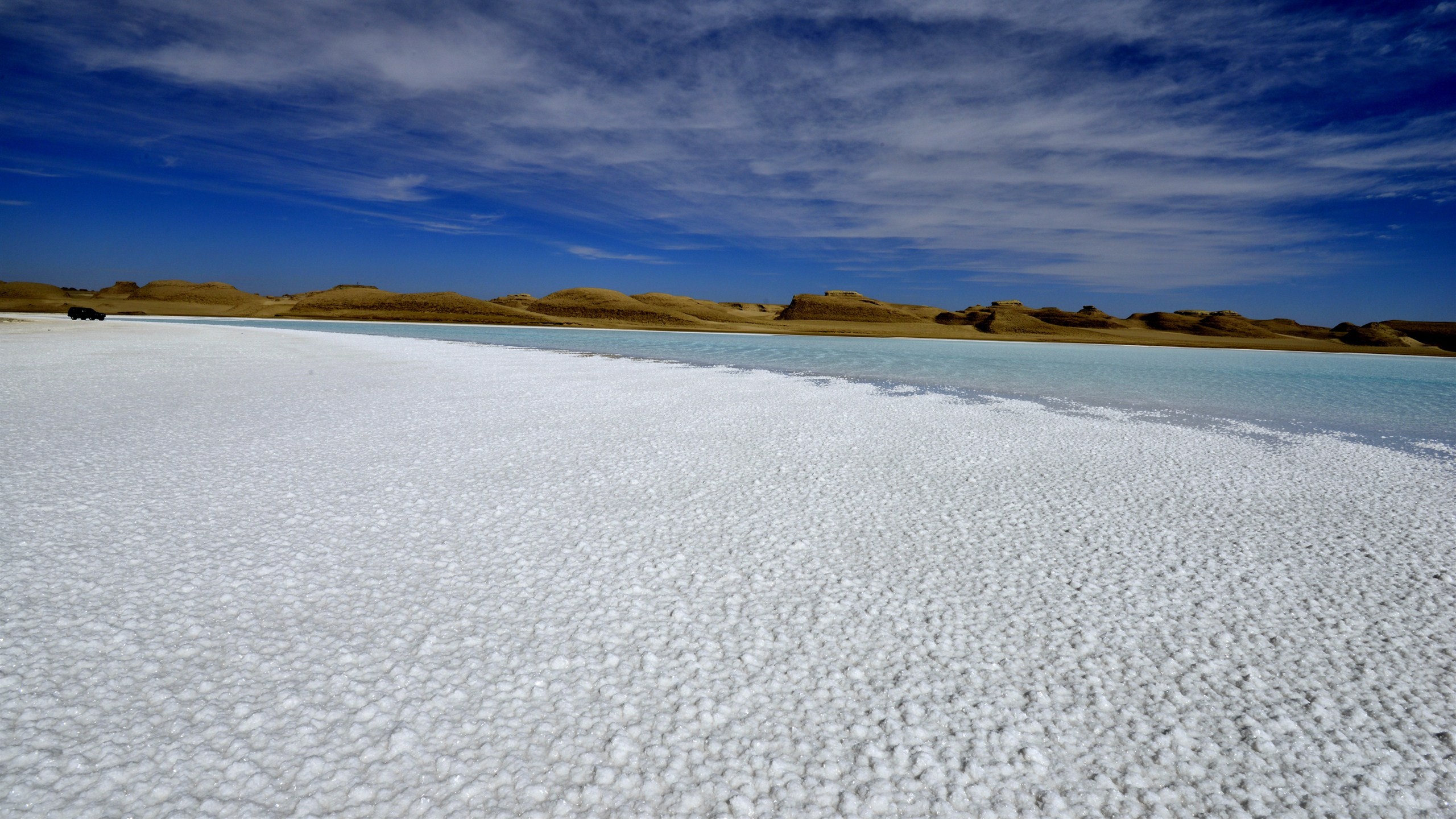 巍巍远山，青青盐湖，白茫茫的盐晶遍地，蓝天下一望无际的盐湖在风力的作用下荡漾盐花
